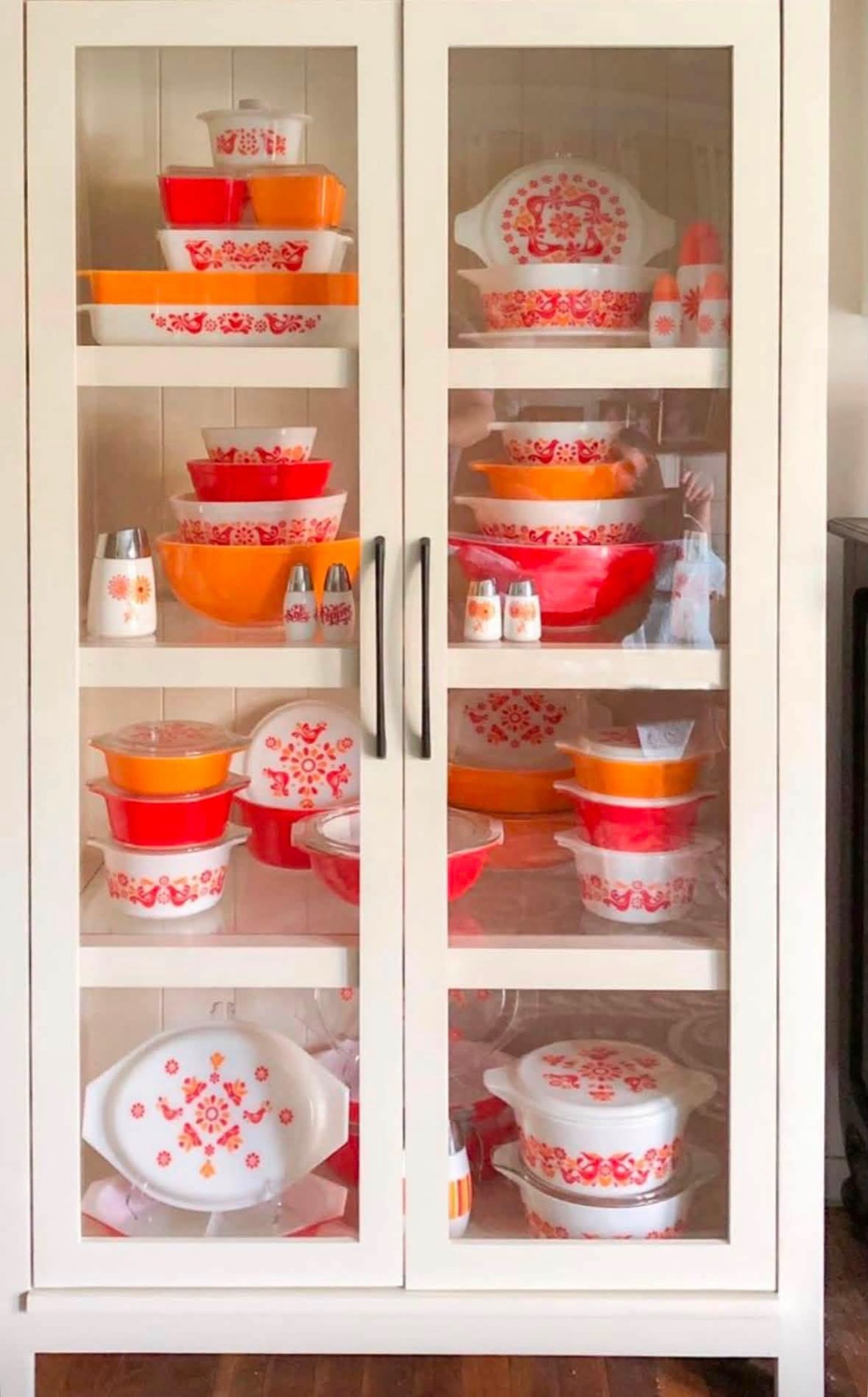 Orange, red, and patterned vintage Pyrex arranged in a white glass-front cabinet